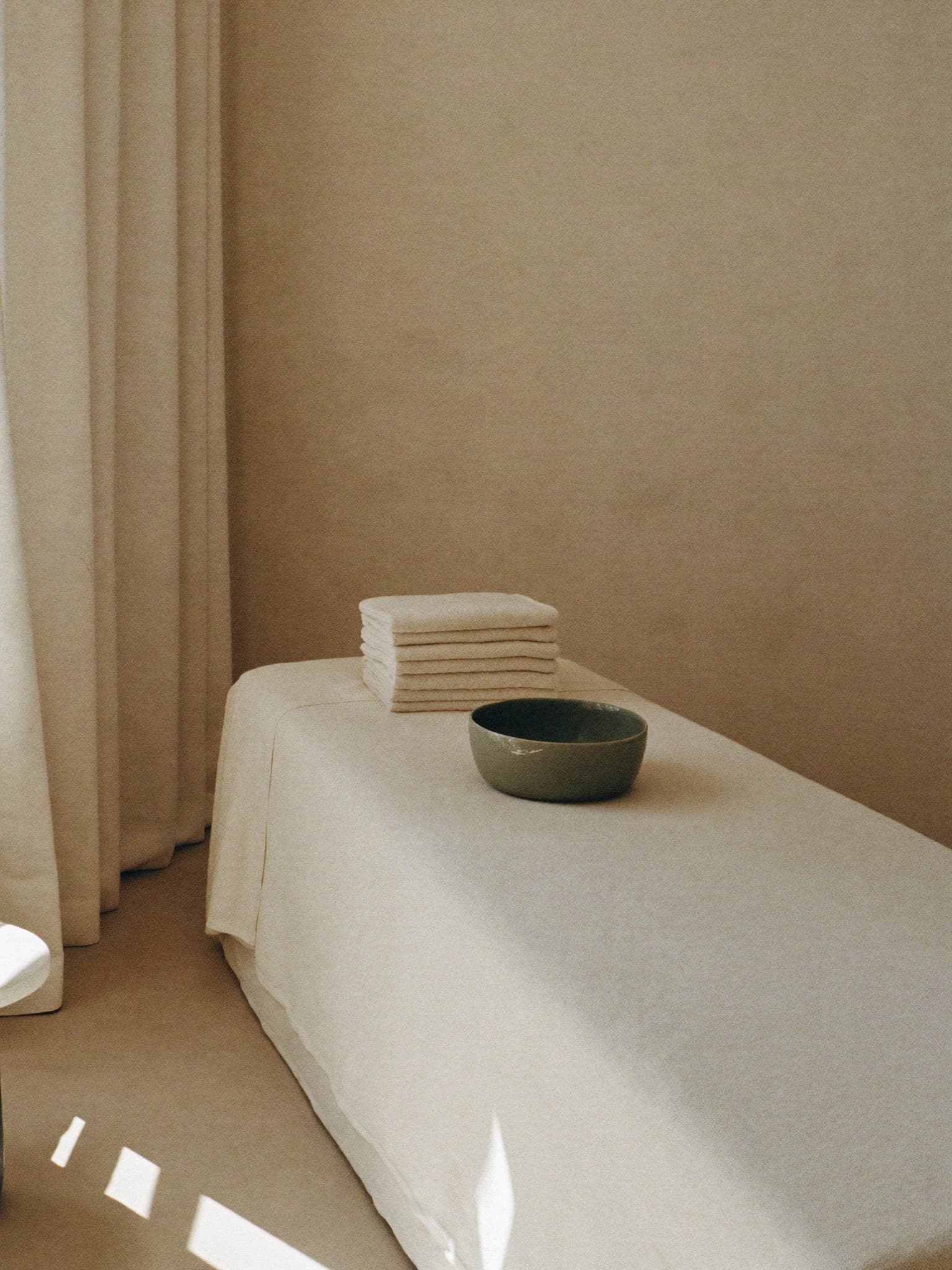 A body treatment room with folded towels stacked at the foot of a linen-covered bed
