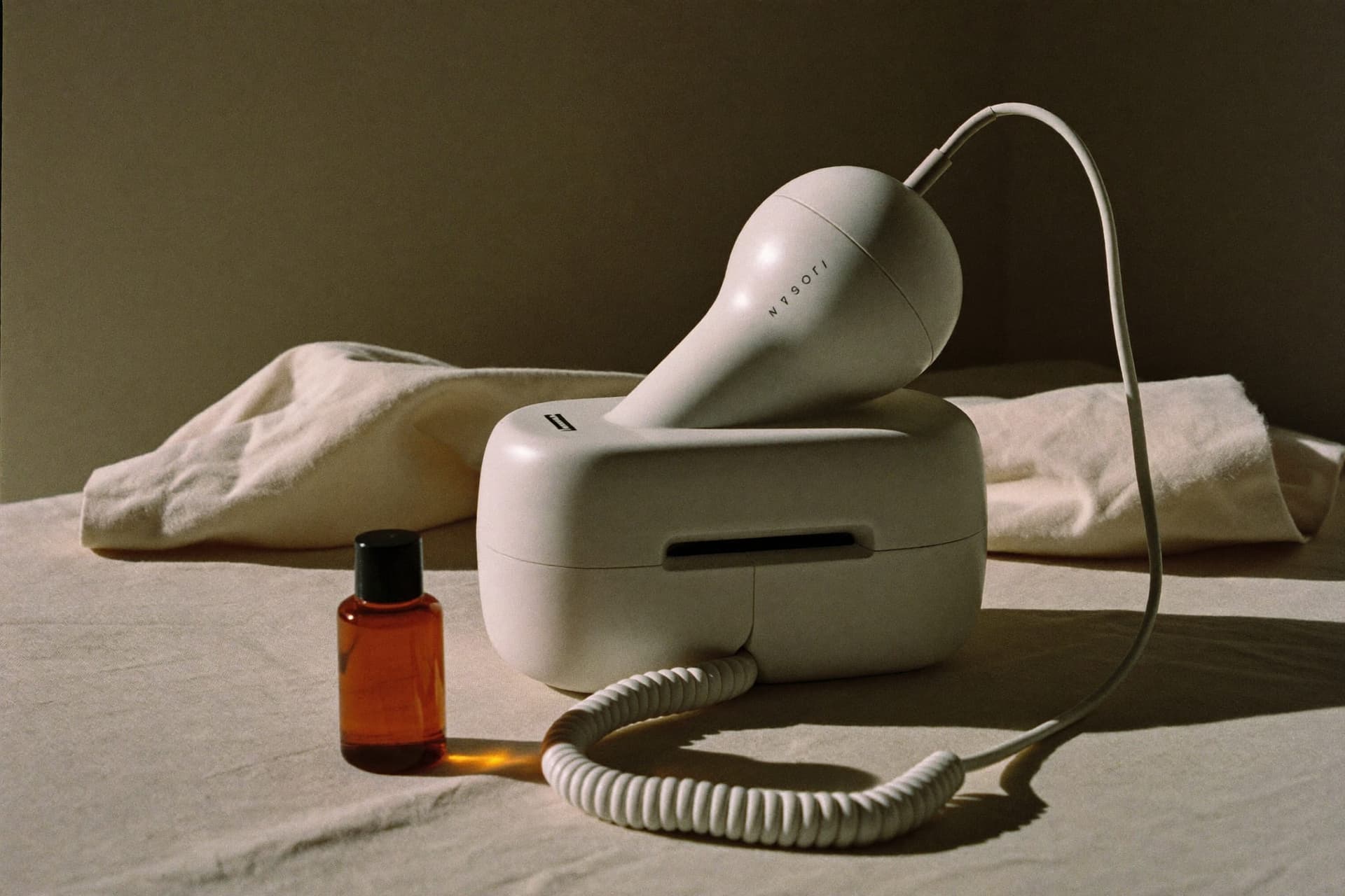 A skincare device handpiece resting on folded linen beside an amber glass bottle